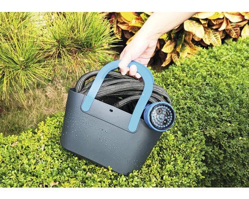 Osoba drží zahradní hadici se zahradní sprchou v košíku před keři.