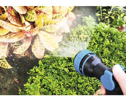 Ruka drží zahradní hadici, která zalévá rostliny.