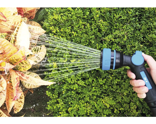 Ruka drží zahradní hadici, která zalévá rostliny.