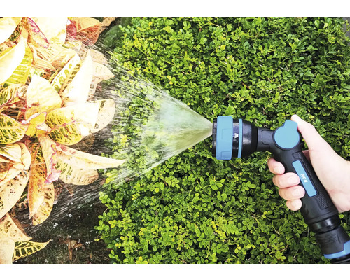 Ruka drží zahradní postřikovač, který stříká vodu na rostliny.