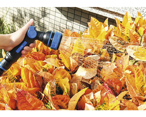 Osoba zavlažuje rostliny zahradní stříkací pistolí.