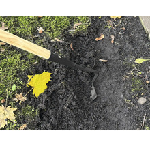 Zahradní motyka s dřevěnou rukojetí používaná na tmavé zemi