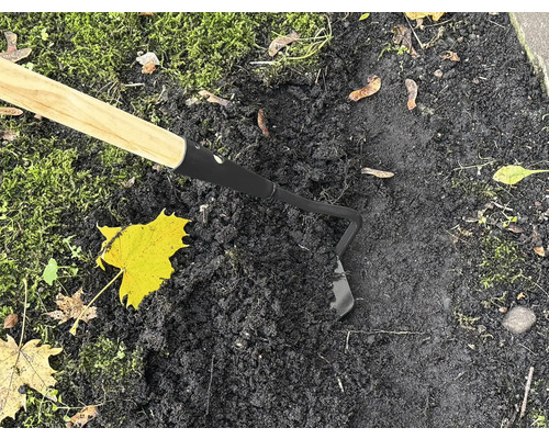 Zahradní motyka s dřevěnou rukojetí používaná na tmavé zemi