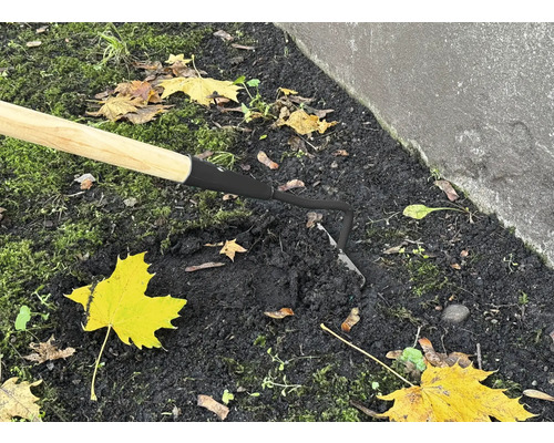 Detailní záběr motyky s dřevěnou rukojetí v zahradní půdě.