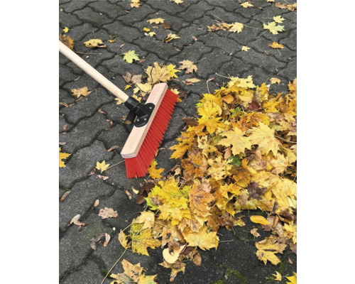 Koště s dřevěnou násadou a podzimní listí na dlažebních kostkách