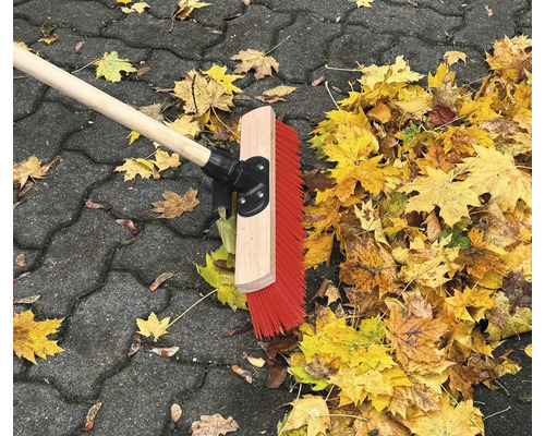 Silniční koště s dřevěnou násadou a podzimní listí na dlažebních kostkách