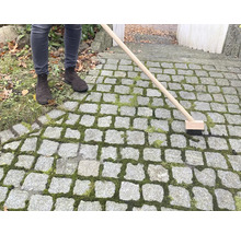 Osoba čistí kamennou dlažbu kartáčem na spáry
