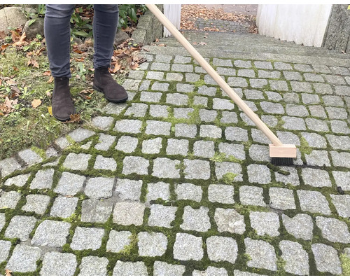 Osoba čistí kamennou dlažbu kartáčem na spáry