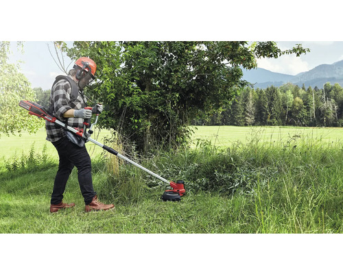 Osoba obsluhující akumulátorový vyžínač v travnatém venkovním prostředí.