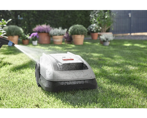 Robotická sekačka je čištěna vodou na trávníku s květinami v pozadí