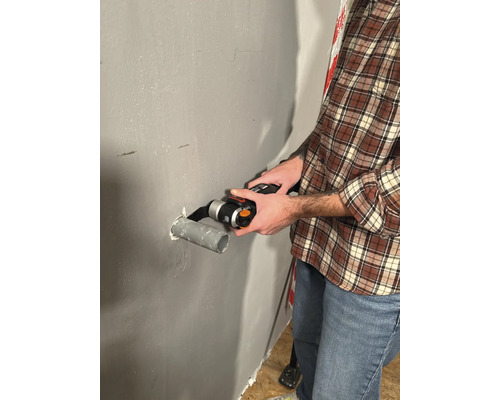 Muž řeže trubku multifunkčním nástrojem na zdi.