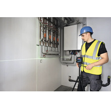 Řemeslník používá čárový laser pro vyrovnání v kotelně.