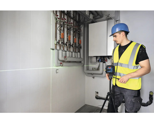 Řemeslník používá čárový laser pro vyrovnání v kotelně.