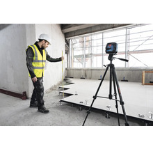 Řemeslník s laserovou vodováhou a nivelační latí při instalaci zdvojené podlahy.