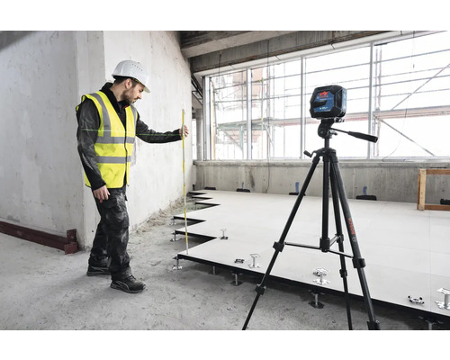 Řemeslník s laserovou vodováhou a nivelační latí při instalaci zdvojené podlahy.