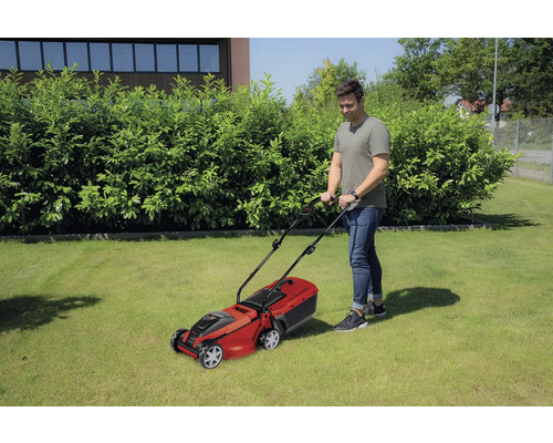 Muž seče trávník sekačkou na trávu na zahradě.