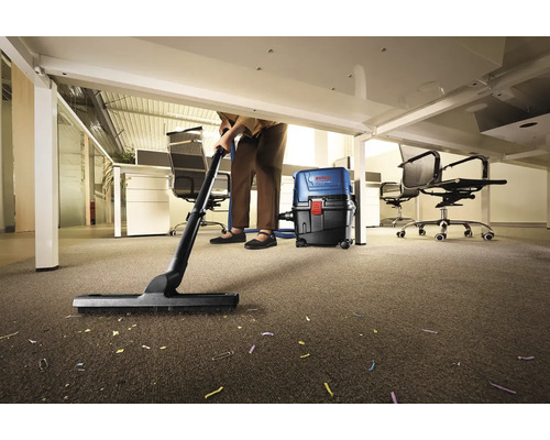 Osoba uklízí vysavačem koberec v kanceláři pod stolem.