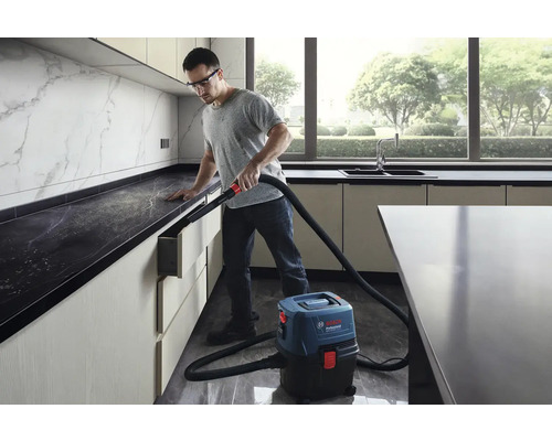 Muž používá mokrý suchý vysavač Bosch Professional v moderní kuchyni k odstranění prachu.