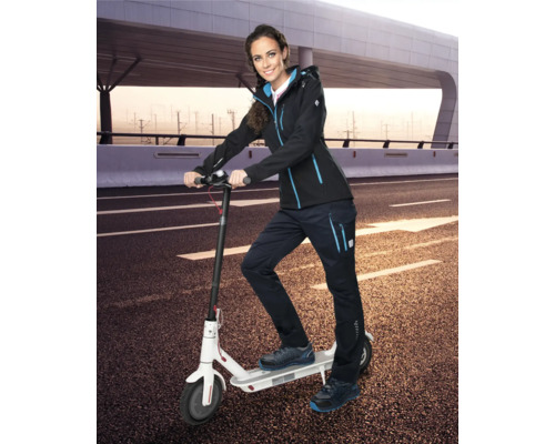 Žena se softshellovou bundou, pracovními kalhotami a bezpečnostní obuví na elektrické koloběžce