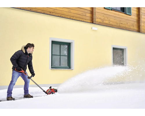 Muž odklízí sníh sněhovou frézou před domem