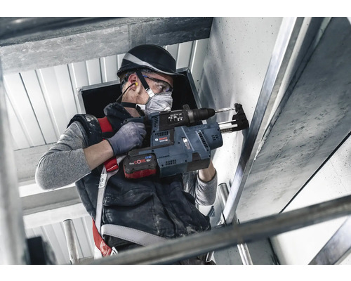 Pracovník vrtá vrtacím kladivem otvor do betonové zdi.