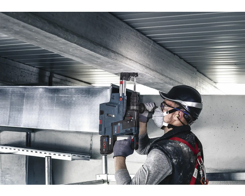 Muž vrtá vrtačkou díru do betonového stropu.