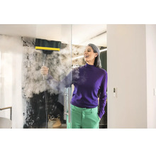 Žena čistí skleněnou stěnu parním čističem v koupelně