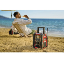 Stavební rádio Einhell na pláži s osobou v pozadí, která si vychutnává pití.