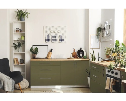 Světlá kuchyně se zelenými skříňkami, dřevěnými pracovními deskami a různými dekorativními předměty