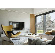 Světlý obývací pokoj s křeslem, pohovkou a okenní fólií s rostlinným vzorem.