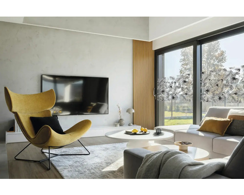 Světlý obývací pokoj s křeslem, pohovkou a okenní fólií s rostlinným vzorem.