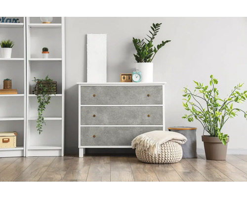 Komoda se třemi zásuvkami, regál a pokojové rostliny ve světlé místnosti.