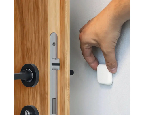 Ruka připevňuje magnetickou zarážku dveří na zeď vedle dřevěných dveří se stříbrným zámkem.