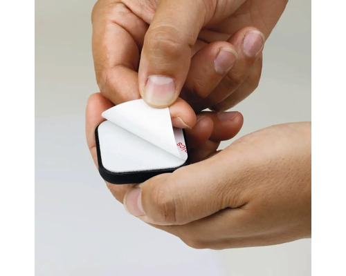 Ruka odstraňuje ochrannou fólii ze samolepicího nábytkového kluzáku.