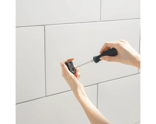 Upevnění černého držáku šroubovákem na obloženou stěnu