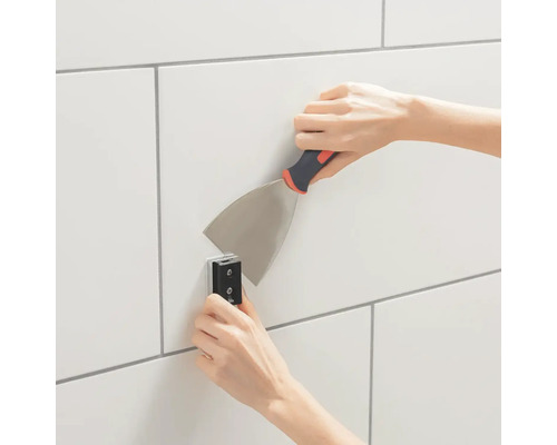 Osoba připevňuje dlaždice na zeď špachtlí