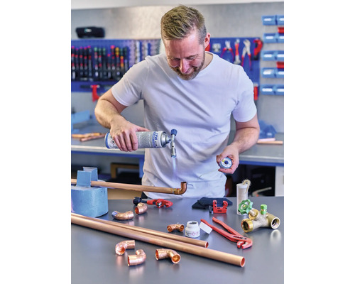 Muž pájí měděné trubky plynovým hořákem a nářadím na stole.