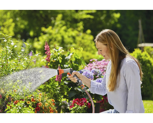 Žena zalévá rostliny zahradní hadicí na zahradě