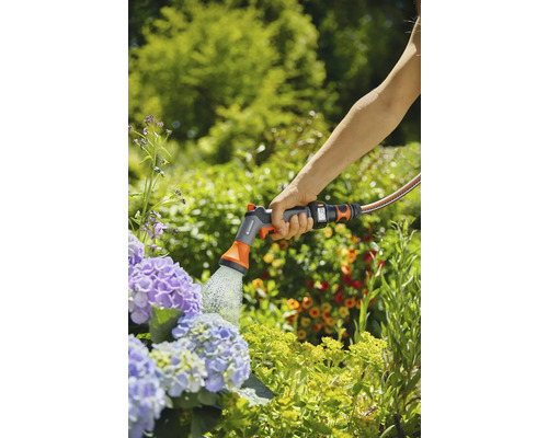 Osoba zalévá květiny zahradním zařízením Gardena.