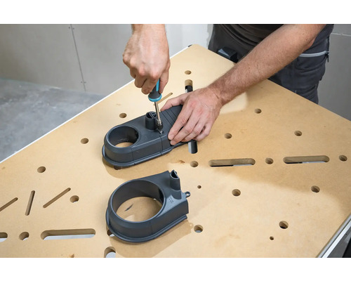 Osoba montuje odsávací nástavec pomocí šroubováku na pracovní stůl