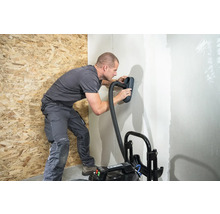 Muž brousí stěnu pomocí brusky a vysavače