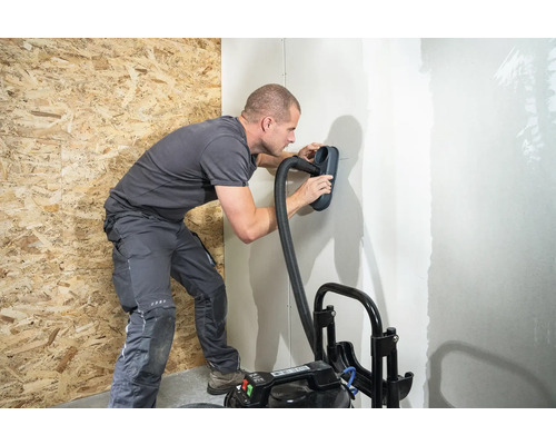 Muž brousí stěnu pomocí brusky a vysavače