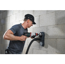 Muž vrtá do zdi vrtačkou a odsáváním prachu.