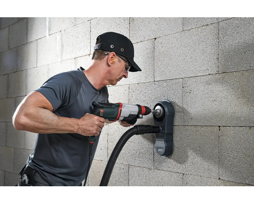 Muž vrtá do zdi vrtačkou a odsáváním prachu.