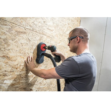 Řemeslník vrtá vrtačkou skrz dřevěnou desku s odsáváním prachu