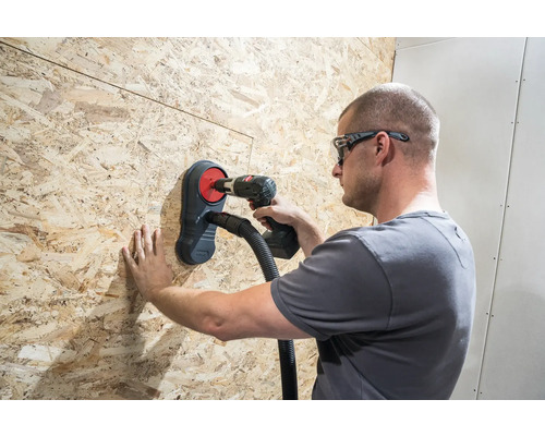 Řemeslník vrtá vrtačkou skrz dřevěnou desku s odsáváním prachu