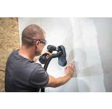 Muž vrtá díru do zdi s nástavcem na vysavač