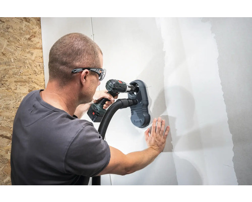 Muž vrtá díru do zdi s nástavcem na vysavač