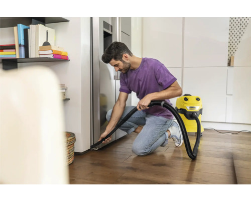 Muž vysává podlahu v moderním domě žlutým víceúčelovým vysavačem.