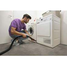 Muž čistí sušičku vysavačem ve světlé prádelně.